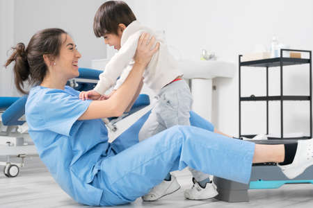 Physiotherapist hugging a little boy with a disability at rehabilitation clinic. Kid with cerebral...