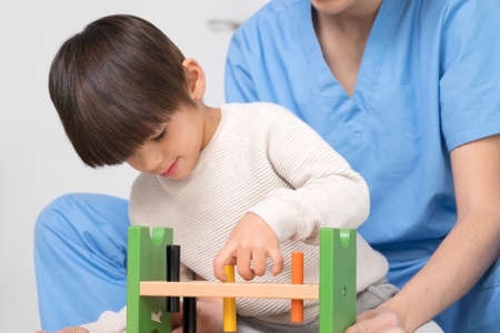 cute kid with disability playing with developing toys while is being helped by physiotherapist in...