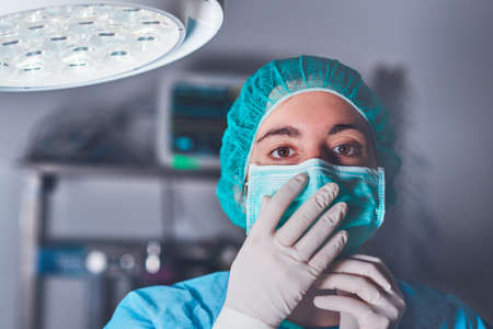 Adult woman in medical mask and hat looking at camera before performing surgery in hospitalの写真素材