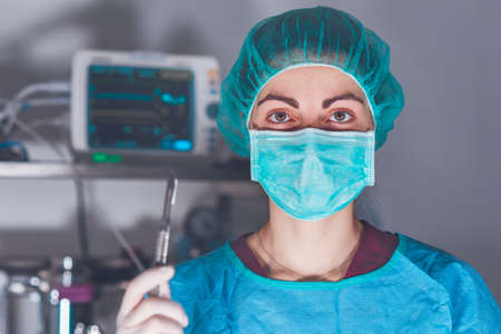 Adult woman in medical mask and hat and with scalpel looking at camera before performing surgery in hospitalの写真素材
