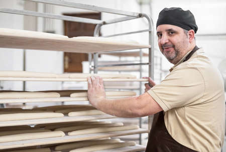 Confident baker posing with rack of fresh bread loaf at bakery.の写真素材