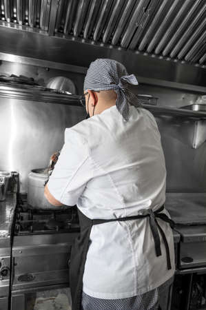 Back view of woman chef cooking food in the kitchen of a restaurant.の写真素材