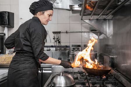 Woman Chef Cooking wok in the Kitchen. Cooking flaming wok with vegetables in the commercial kitchen.の写真素材