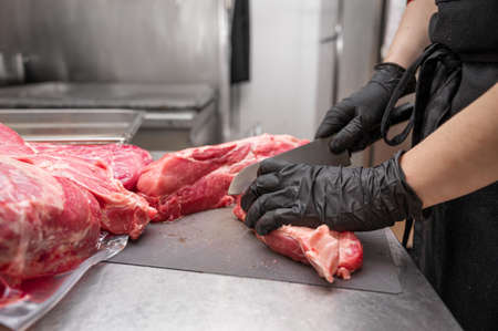 Close up of raw meat and woman butcher cutting meat with knife.の写真素材