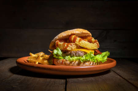 Premium quality burger with onion rings, cheese and barbecue sauce, served with french fries on a rustic plateの写真素材