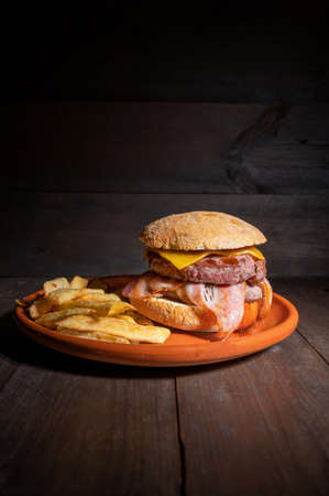 Premium grilled beef hamburger with bacon, cheese and French fries. Delicious American burger on wooden background.の写真素材