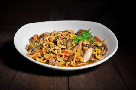 Asian vegetarian food udon noodles with shiitake mushrooms, sesame and pepper close-up on a plate on the wooden table.の写真素材