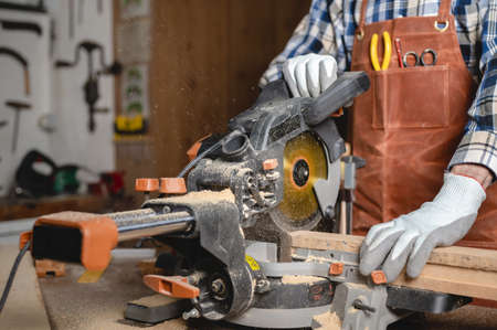Carpenter using an electric circular saw, cutting piece of wood.の写真素材