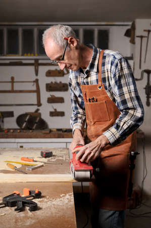 Carpenter sanding wood with belt sander at workshop in wooden board project or woodworking carpentryの写真素材