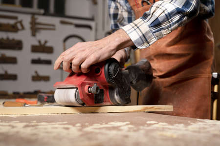 Carpenter sanding wood with belt sander at workshop in wooden board project or woodworking carpentryの写真素材