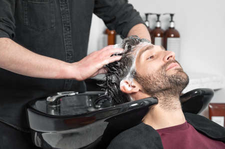 Barber shop. Hairdresser man washes client head in barbershopの写真素材