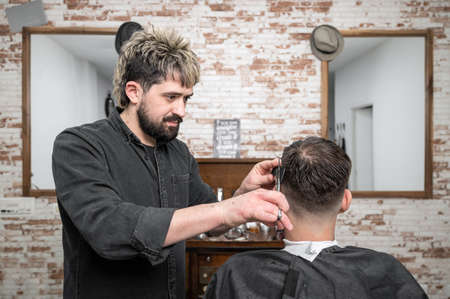 Barber cutting hair with scissors to a handsome young man .の写真素材