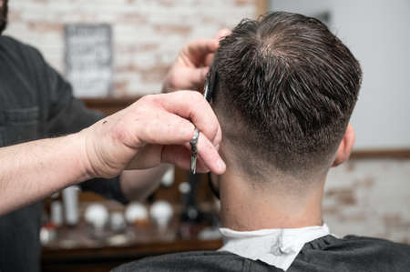Barber cutting hair with scissors to a handsome young man .の写真素材