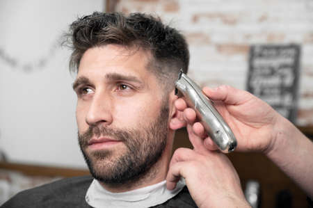 Man barber cutting hair of male client with clipper at barber shop. Hairstyling process.の写真素材