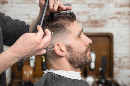 Barber cutting hair with scissors to a handsome young man .