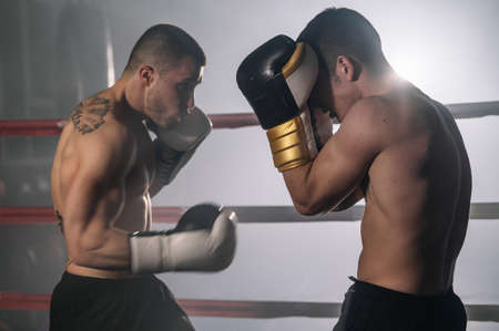 Two professional young muscular shirtless male boxers fighting in a boxing ring.の写真素材