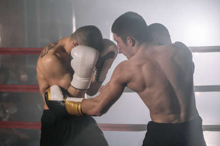 Two professional young muscular shirtless male boxers fighting in a boxing ring.の写真素材