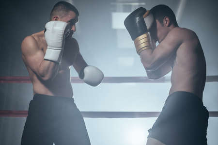 Two professional young muscular shirtless male boxers fighting in a boxing ring.