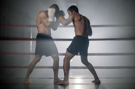 Two professional young muscular shirtless male boxers fighting in a boxing ring.の写真素材