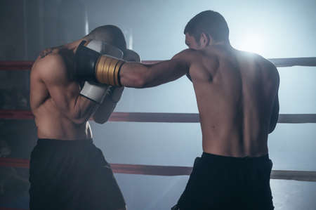 Two professional young muscular shirtless male boxers fighting in a boxing ring.