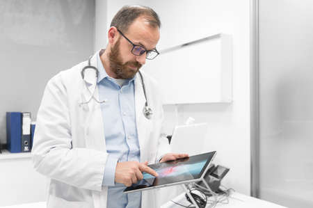 Doctor examine an x-ray image of a patient in digital tablet at doctor office.の写真素材
