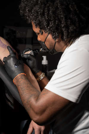 Professional African American tattoo artist makes a tattoo on client armの写真素材