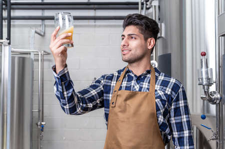 Handsome brewer in apron testing beer at brewery.の写真素材