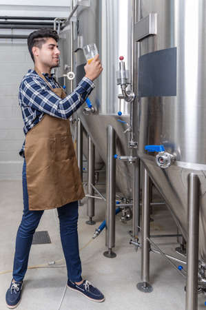 Handsome brewer in apron testing beer at brewery.の写真素材