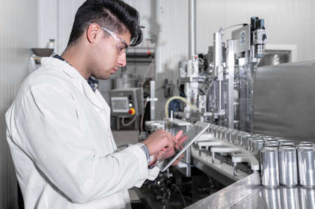 Factory worker inspecting production line on beverage factory with computer tablet.