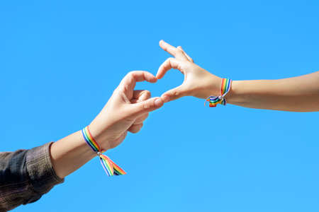 Close up of Woman hands in a rainbow bracelet making a heart shape form on blue sky background.の写真素材