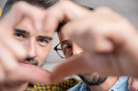 Young gay couple smiling confident doing heart symbol with hands at home