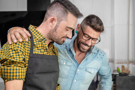 Happy hipster gay couple in love standing in the kitchen. They are cooking dinner together at home.の写真素材