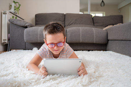 Cute little boy watch cartoons on digital tablet. Kid lies on floor laughing using electronic device. Indoor leisure for children.の写真素材