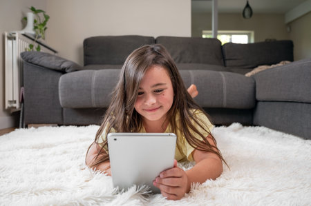 Adorable little girl using a digital tablet on the floor at home.の写真素材