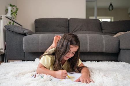Cheerful little girl lying on the floor drawing.の写真素材