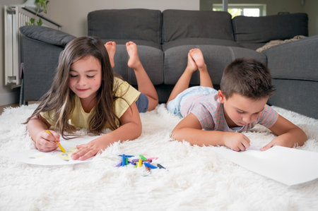 Siblings playing together at home. little boy and girl lying on the carpet and drawing on white sheets of paper with colorful crayonsの写真素材