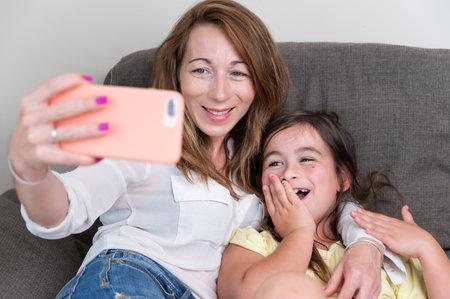 Happy mother with her daughter are making a video call to father or relatives in a sofa. Concept of technology, new generation, family, connection, parenthood.の写真素材