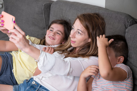 Happy mother with her kids are making a selfie or video call to father or relatives in a sofa. Concept of technology, new generation, family, connection, parenthood.の写真素材
