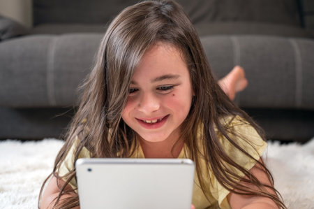 Adorable little girl using a digital tablet on the floor at home.の写真素材