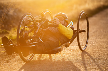 Scenic Shot of a Young Man Athlete with disability Riding a Handcycle. Adaptive Exercise Outdoors at Sunsetの写真素材