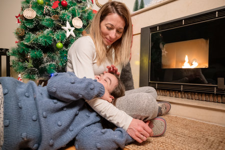 Mother and daughter hugging and smiling, winter evening together at home in a decorated living room at Christmas Eve. Family happynessの写真素材