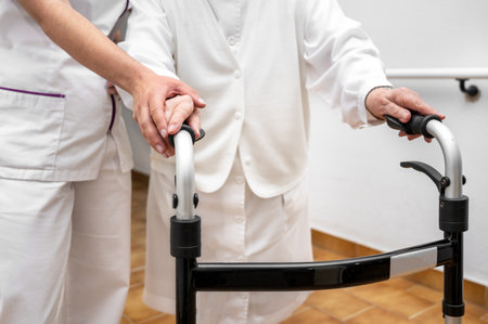 Nurse assists her senior patient on folding walker. Recuperation for elderly, seniors care, nursing home.の写真素材