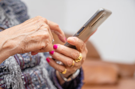 Elderly woman with smartphone, mobile phone in wrinkled female hands, close up. Concept of online communication in retirement.の写真素材