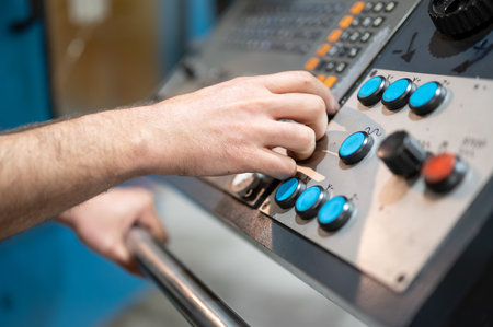 Worker pressing buttons on CNC machine control board in factory.