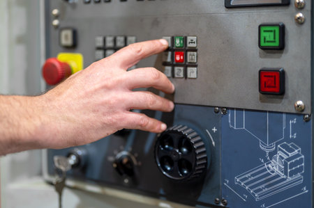 Worker pressing buttons on CNC machine control board in factory.