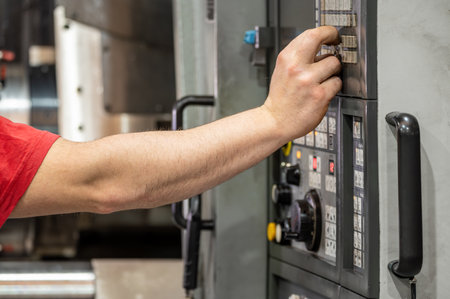 Worker pressing buttons on CNC machine control board in factory.の写真素材