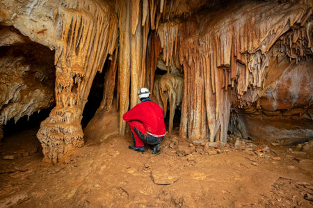 A speleologist with helmet and headlamp exploring a cave with rich stalactite and stalagmite...