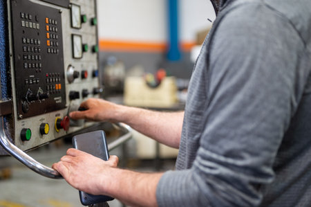 Worker pressing buttons on CNC machine control board in factory.