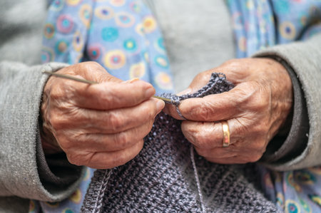 Close up of a mature woman knitting at home, enjoying leisure time, holding needles, elderly generation hobby activity.の写真素材