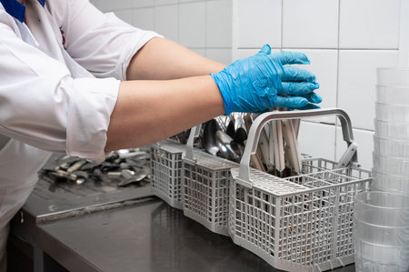 Unrecognizable woman, preparing dirty cutlery for washing at the dishwasher in commercial kitchen